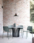 Modern outdoor dining set with a round table and chairs against a brick wall and Masiero's Cordea outdoor pendant light