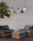 Outdoor furniture set with wicker chairs and ottoman against a tiled wall with hanging pendant lights.