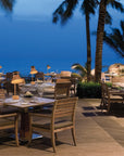Outdoor dining area with tables and chairs under palm trees at dusk and Masiero's Cordea rechargeable table lamps on each table.