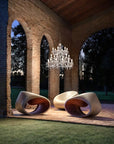 Modern outdoor chairs under an outdoor chandelier from Masiero's Drylight collection in an archway with trees in the background