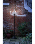 Decorative outdoor floor lamp with crystal fixture against a brick wall.