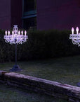 Two illuminated chandelier lights on stands in a garden setting with a dark background.