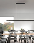 Modern dining room with a long wooden table and chairs, featuring a black pendant Kinetic light.