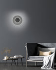 Modern wall light fixture on a dark gray wall with a sofa and coffee table in the foreground.