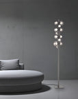Modern floor lamp with multiple bulbs next to a round gray sofa against a gray wall.
