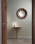 Decorative round mirror on a wall with a small table and lamp in a room.