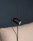 Modern black floor lamp against a dark blue wall with a beige sofa.