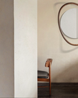 Round mirror with wooden frame on a wall next to a chair.