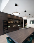 A modern kitchen and dining space with dark wood cabinetry, a long dark wood island table, teal chairs, and three round pendant lights hanging from a white ceiling.