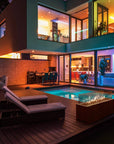 Modern house exterior with pool, lounge chairs, and fire pit at night.