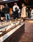 People gathered around a fire pit on a brick patio with a building in the background