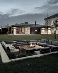 Modern outdoor seating area with a gas fireplace in a garden setting at dusk.