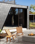 Modern outdoor setting with a fire pit, chairs, and a building with a glass wall.