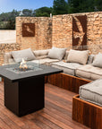 Outdoor patio with sectional sofa and fire pit table against a stone wall.