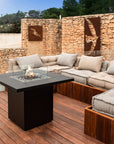 Outdoor patio with sectional sofa and fire pit table against a stone wall.