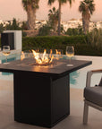 Outdoor patio setup with fire pit table, chairs, and decorative pillows by a pool.