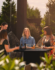 People sitting around a gas fireplace table with drinks in an outdoor setting