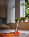 Orange water tank of Planika artificial water vapour fireplace with water flowing from a silver faucet in a kitchen setting.