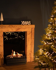 Planika Basket fire place with logs in a wooden fireplace mantle with christmas tree and decorations.
