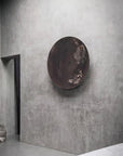 Round metallic glass wall art piece on a textured gray wall