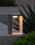 Modern outdoor indoor solar lantern with a concrete base and glass cover, illuminated in a garden setting by Les Jardins available at Spacio retail stores in India.