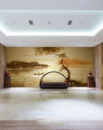 Golden watercolour fresco mural depicting a calm lake, a small boat, and a windswept tree, handcrafted on Italian plaster with Carrara marble and travertine powder. Featured on a wall in a hotel lobby in front of a modern design basket sofa