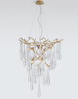 A Serip Aqua Chandelier from the Serip brand, crafted with gold and crystal materials, hangs elegantly from a white wall.