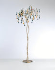 A floor lamp with glass droplets hanging from golden branch on a light grey colour background