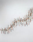 A grand wall light installation with colourful glass icicles hanging from metal branches in the shape of a wave on the wall on a light grey colour background.