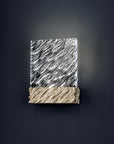Decorative wall light with patterned glass top and textured gold base on a dark background