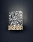 Decorative wall light with patterned glass top and textured gold base on a dark background
