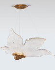 Decorative sculptural hanging light in leaf shape made of brass and glass with gold accents on a white background