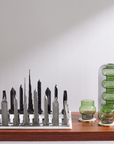 Skyline Chess Steel Dubai Marble Carrara Board styled along with luxury glass artefacts on a wooden table by interior stylist navin kanodia, available at Spacio online and retail stores in India