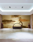Golden watercolour fresco mural depicting a calm lake, a small boat, and a windswept tree, handcrafted on Italian plaster with Carrara marble and travertine powder. Featured on a wall in a hotel lobby in front of a modern design basket sofa