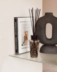 A Baobab Arabian Nights Diffuser with a woody fragrance graces a shelf alongside a book available at Spacio India for luxury home decor collection of Candles & Frangrace.