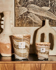 A collection of Baobab Sand Siloli candles on a shelf next to a painting.