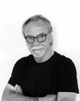 A black and white photo of a man with glasses wearing an Italamp Pulsa Spira illumination chandelier as a headpiece.