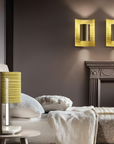 A bedroom with a yellow Masiero Ebe Wall Sconce from the Masiero Ebe Collection, illuminating the space with its luxury lighting and creating a cozy atmosphere alongside a fireplace.
