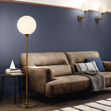 A living room with blue walls and a brown couch adorned with a Masiero Tee Floor Lamp.
