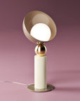 A versatile and vibrant lighting design from the Aurora Collection by Italamp featuring brushed gold accents, white glass diffuser, and retro-inspired finishes. Close up of an ivory finish table lamp on a pink background