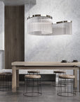 Discover the Carmen collection by Italamp – Italian Murano glass lighting in clear, smoke, and teak finishes. Elegant designs for luxurious interiors. A spiral chandelier in a clear finish on a wooden dining table in a minimal japandi theme interior