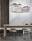 Discover the Carmen collection by Italamp – Italian Murano glass lighting in clear, smoke, and teak finishes. Elegant designs for luxurious interiors. A spiral chandelier in a clear finish on a wooden dining table in a minimal japandi theme interior