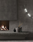 Colier collection by Italamp, featuring modular blown glass elements in vibrant colours and shapes, designed by Marc Sadler to create magical lighting effects. Set on a dark theme interior on the wall next to a fireplace and art objects