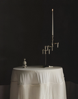 A tall silver candelabra with multiple arms stands on a round table draped in a white table skirt against a dark black background.