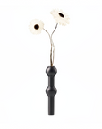 A matte black metal vase with a double-bulb design holding two white daisy-like flowers with dark centers, set against a solid white background.