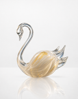 A decorative crystal swan figurine with a curved neck, clear glass body, and subtle gold flecks, displayed on a reflective white surface against a light gray background.