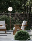 Outdoor setting with wooden chairs, a floor lamp, and greenery.