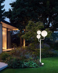 Modern outdoor lamp from Maserio in a garden setting with a house in the background