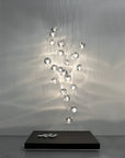 A cluster of Terzani Mizu Pendant Italian crystal light in clear finish above a floor coffee table with white pebbles showing water reflections on the wall. Available at Spacio retail stores in Mumbai & Kolkata.