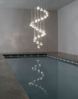 Terzani Mizu Pendant Italian crystal light in a spiral installation above a water body in a luxury villa. Available at Spacio retail stores in Mumbai & Kolkata.